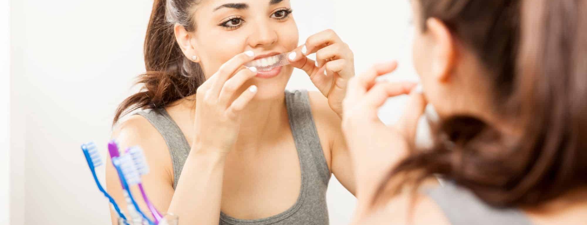 A young woman using a teeth whitening strip (image by AntonioDiaz, Adobe Stock)